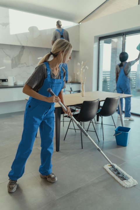 Blonde woman in blue jumpsuit mopping the floor